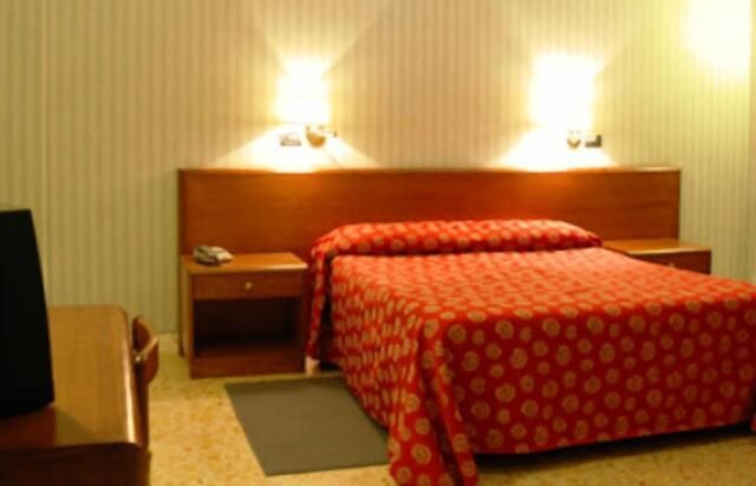 A hotel room with a bed, bedside tables, a desk, and two wall-mounted lamps.