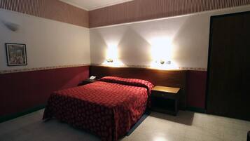 Quarto de hotel com cama, mesa de cabeceira e luminária fixada na parede.