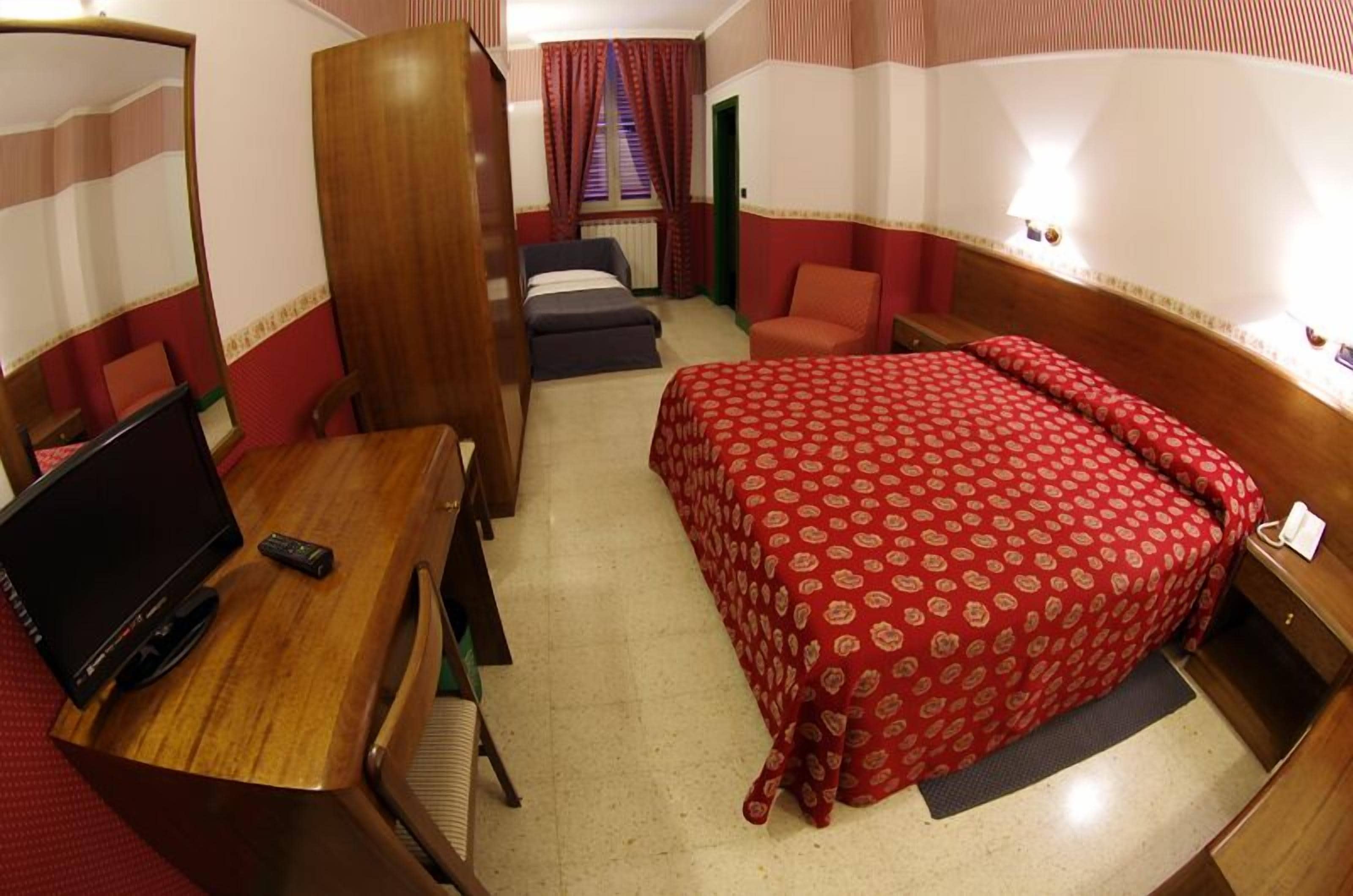 Habitación de hotel pequeña con una cama individual, un escritorio con televisor, una silla y un armario.