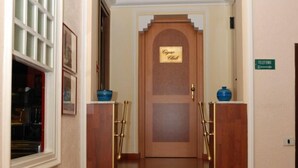 Entrada de hotel con una escalera de madera, mostrador de recepción y un letrero que indica un teléfono.