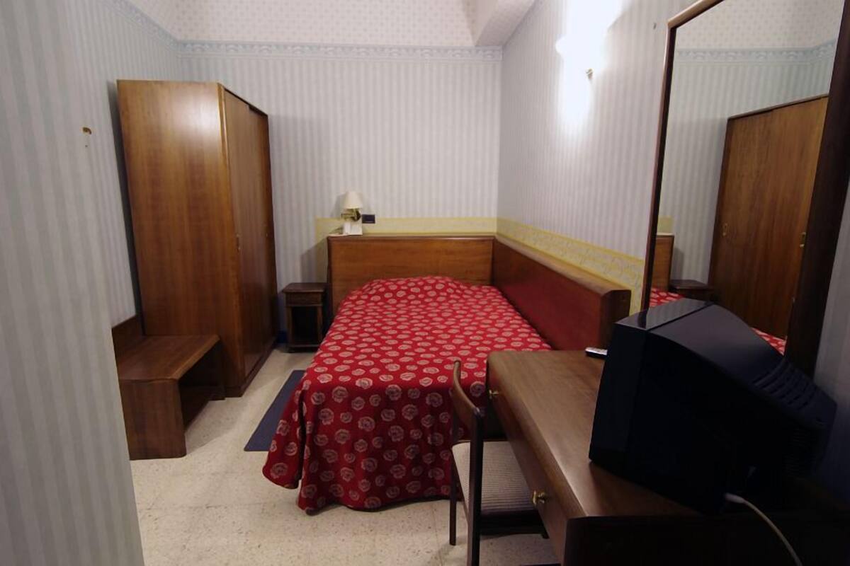 A hotel room with a bed, a desk, a chair, a wardrobe, and a mirror.