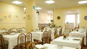 Un comedor con varias mesas dispuestas para el servicio, sillas de madera y una escalera que conduce a un nivel superior.