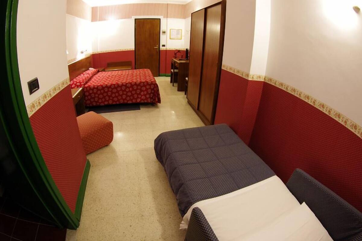 A compact hotel room with two single beds, a desk, and a chair.
