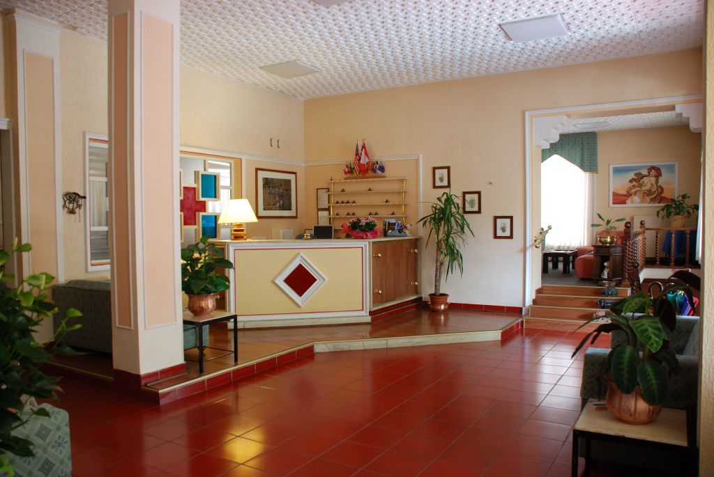 Un hall d’entrée spacieux, doté d’un comptoir de réception, de plantes en pot et d’un escalier menant à un autre espace.