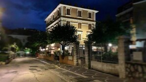 Un immeuble de deux étages doté d’un balcon, avec un arbre devant et une rue pavée.