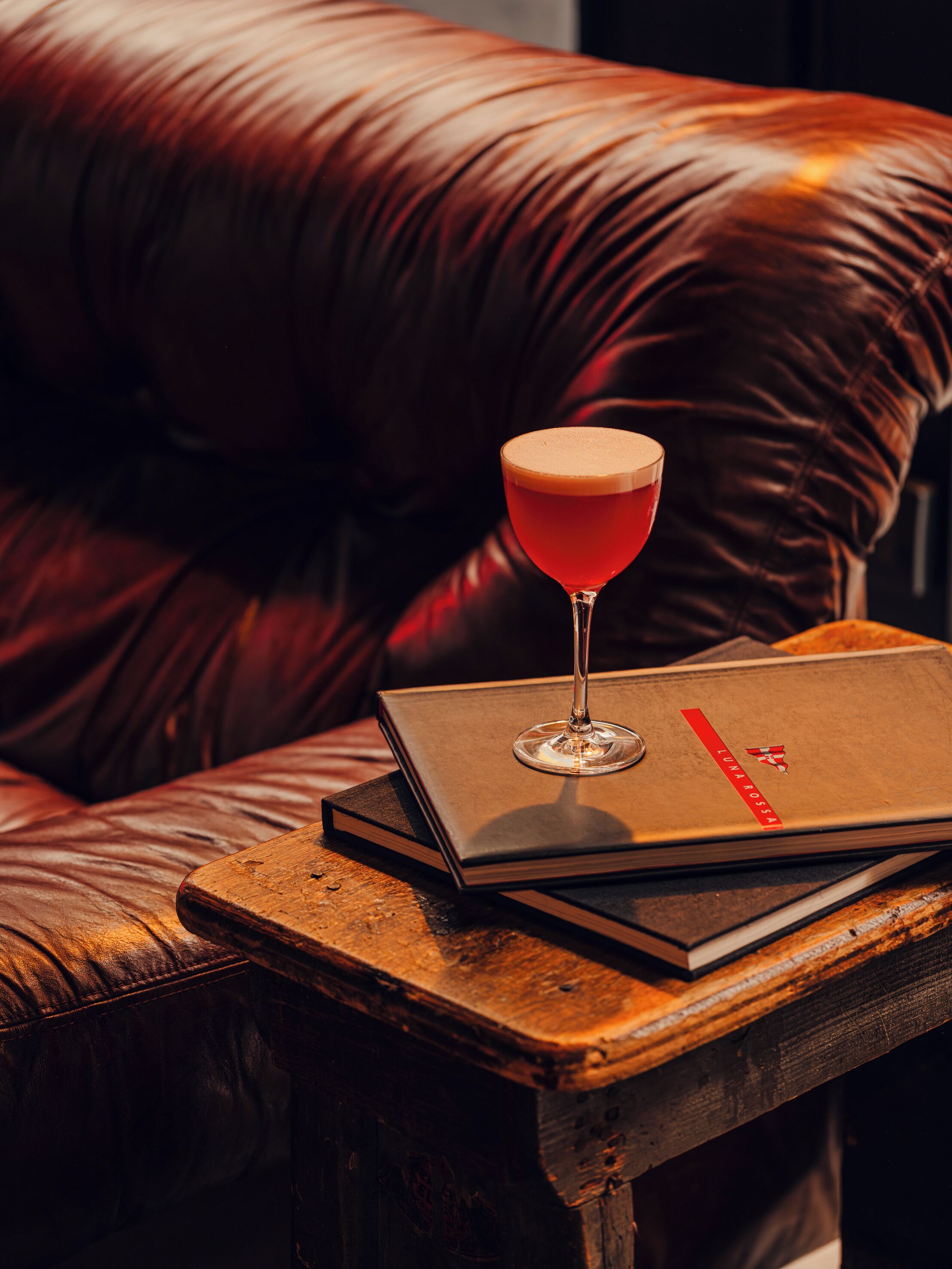 Ein Ledersofa mit einem Glas roter Flüssigkeit und einem Buch auf einem Holztisch.