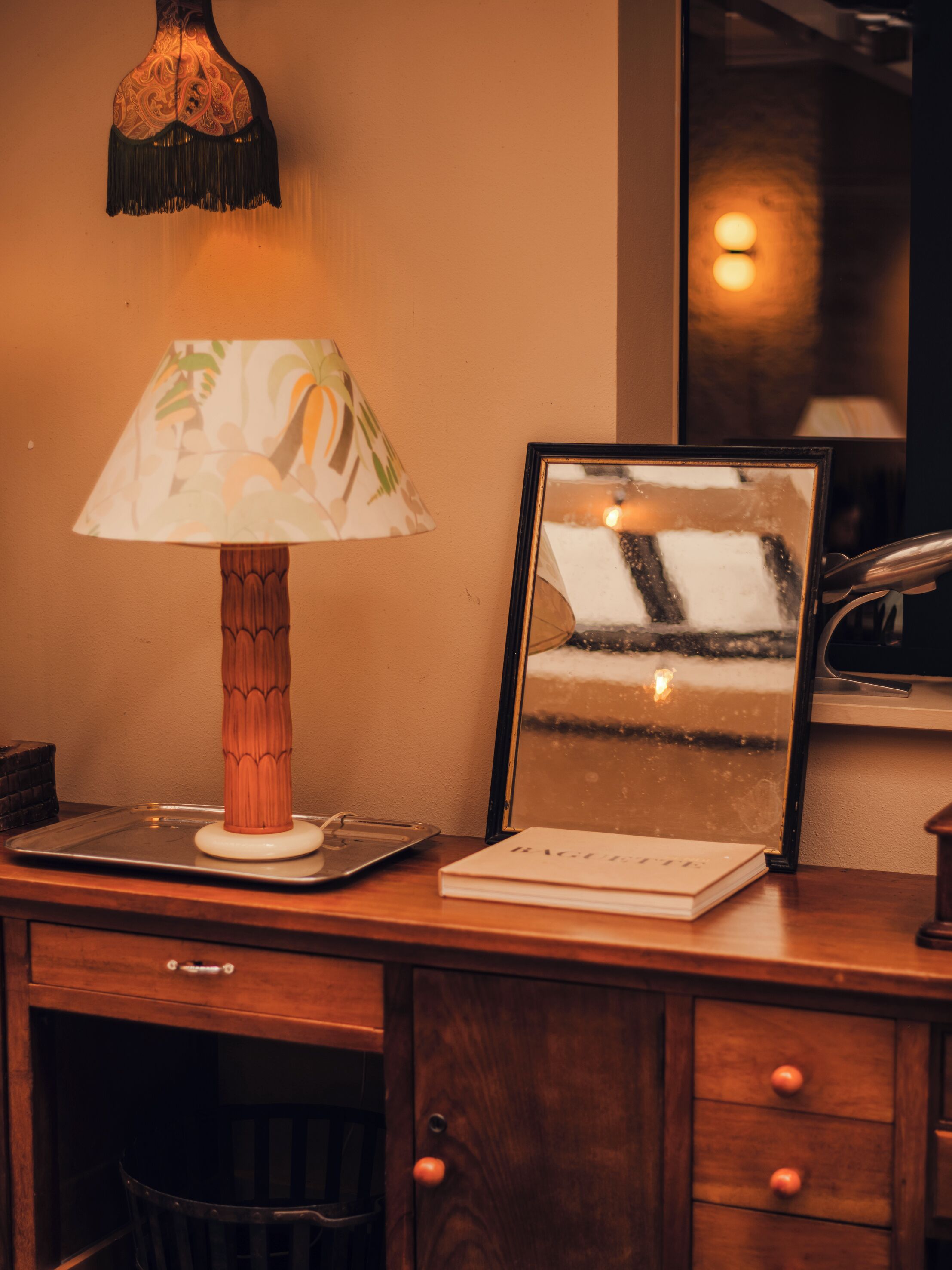 Un bureau en bois, une lampe, un miroir encadré et un livre.