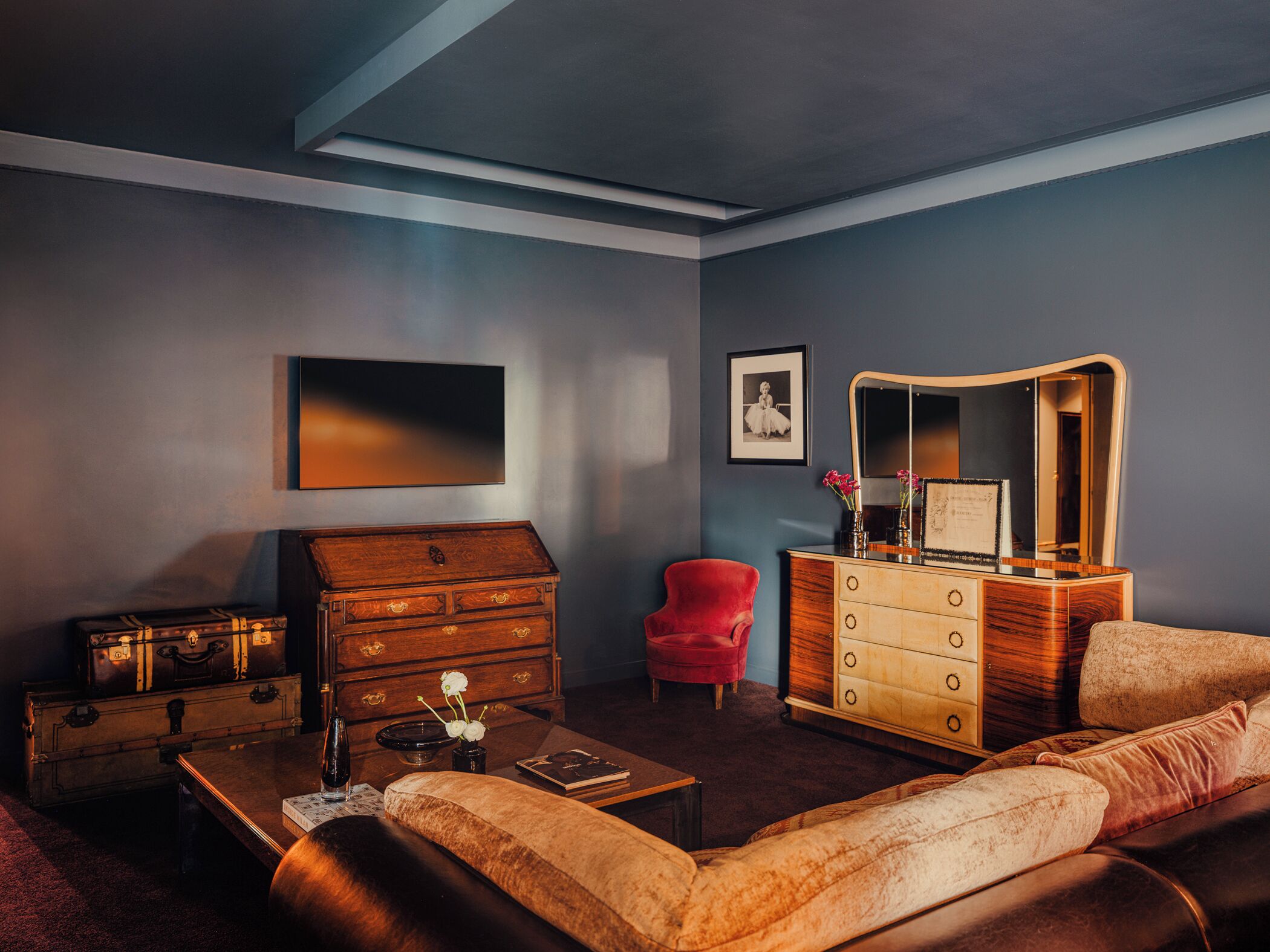 A room with a wooden dresser, a red chair, a sofa, a coffee table, and a framed picture on the wall.