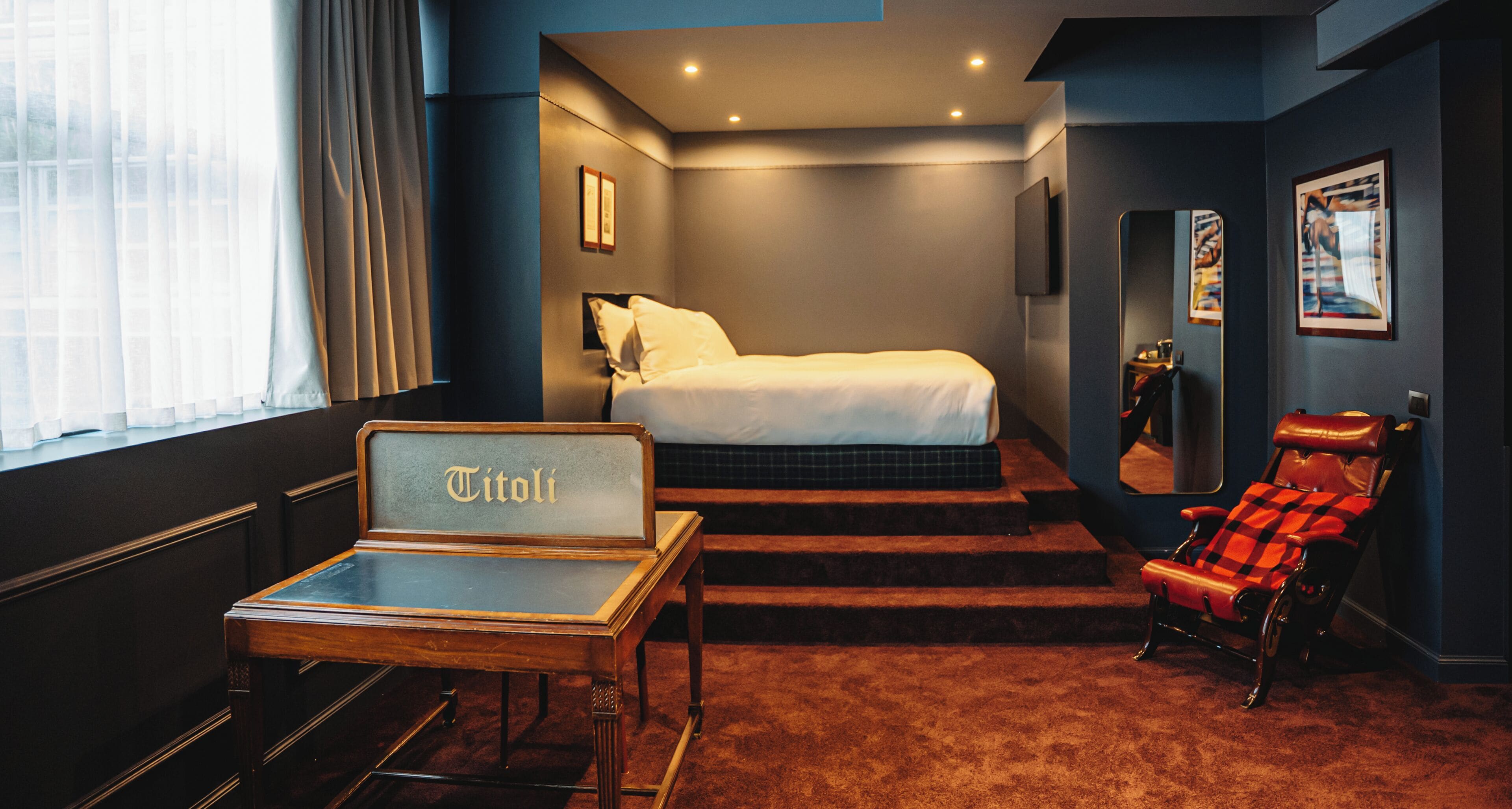 A hotel room with a bed, a desk, a red armchair, and a staircase leading to the bed.