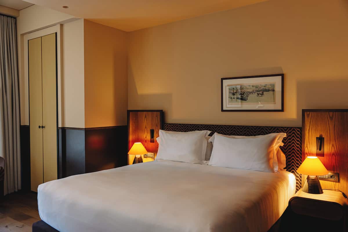 A hotel room with a large bed, two bedside tables with lamps, a framed picture on the wall, and a wardrobe.