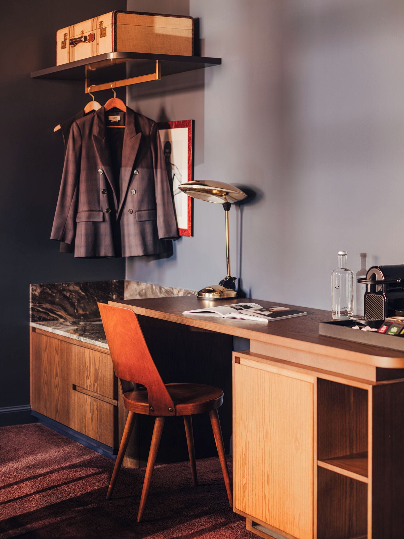 A compact, modern kitchen with a wooden countertop, a single chair, a desk, and a hanging coat rack.
