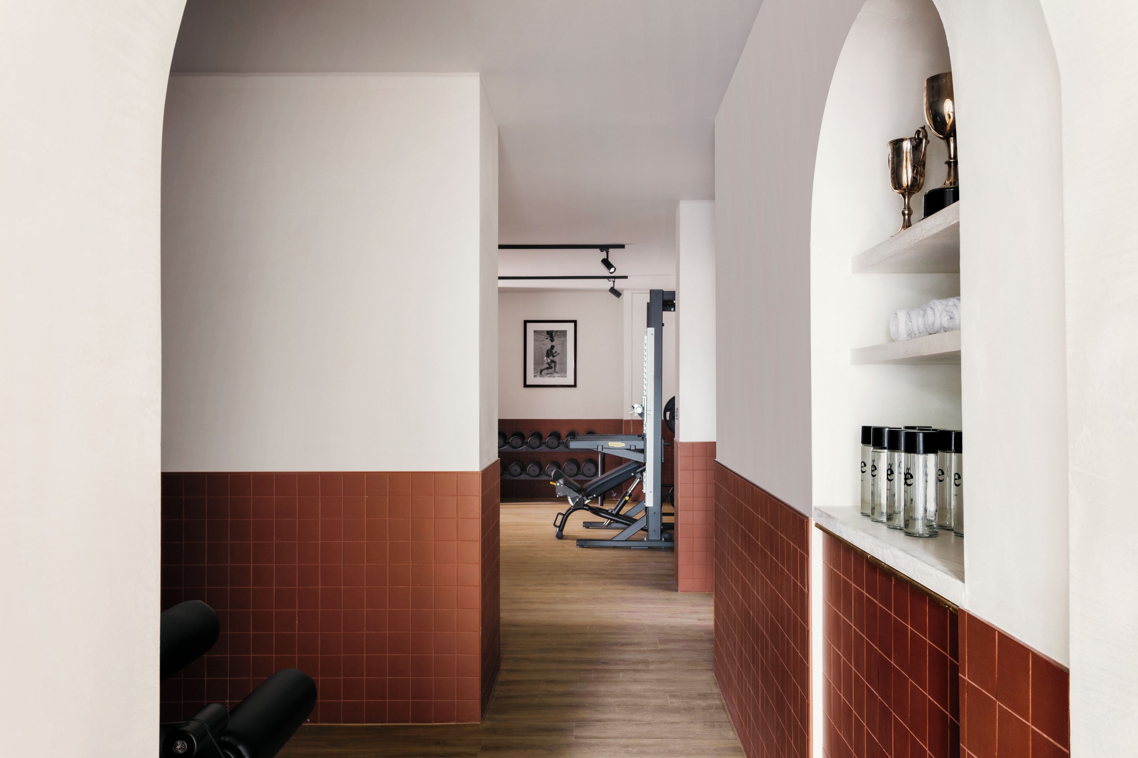 A gym with exercise equipment, a wall-mounted rack of dumbbells, and a shelf with containers.