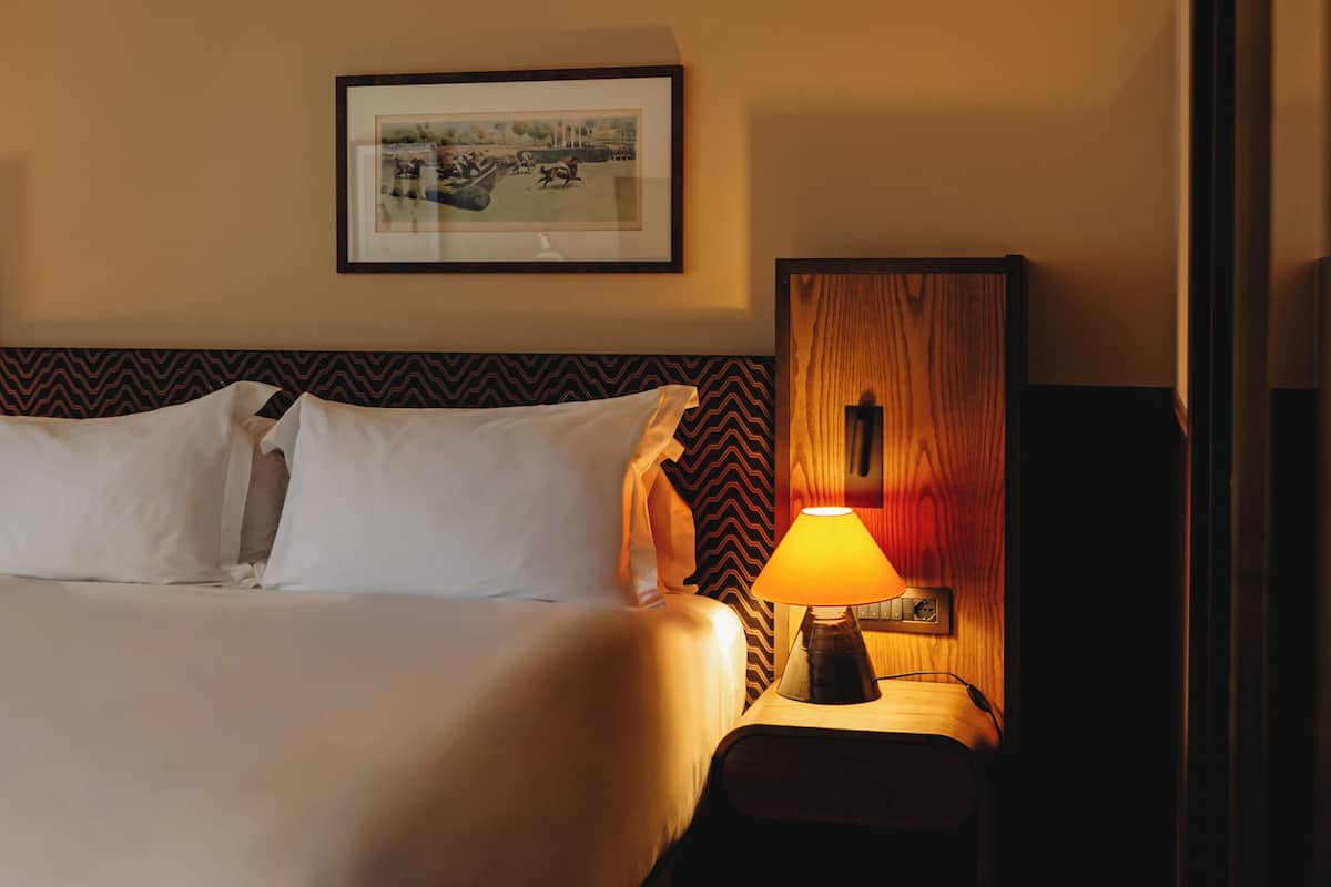 A hotel room with a large bed, a nightstand with a lamp, and a framed picture on the wall.