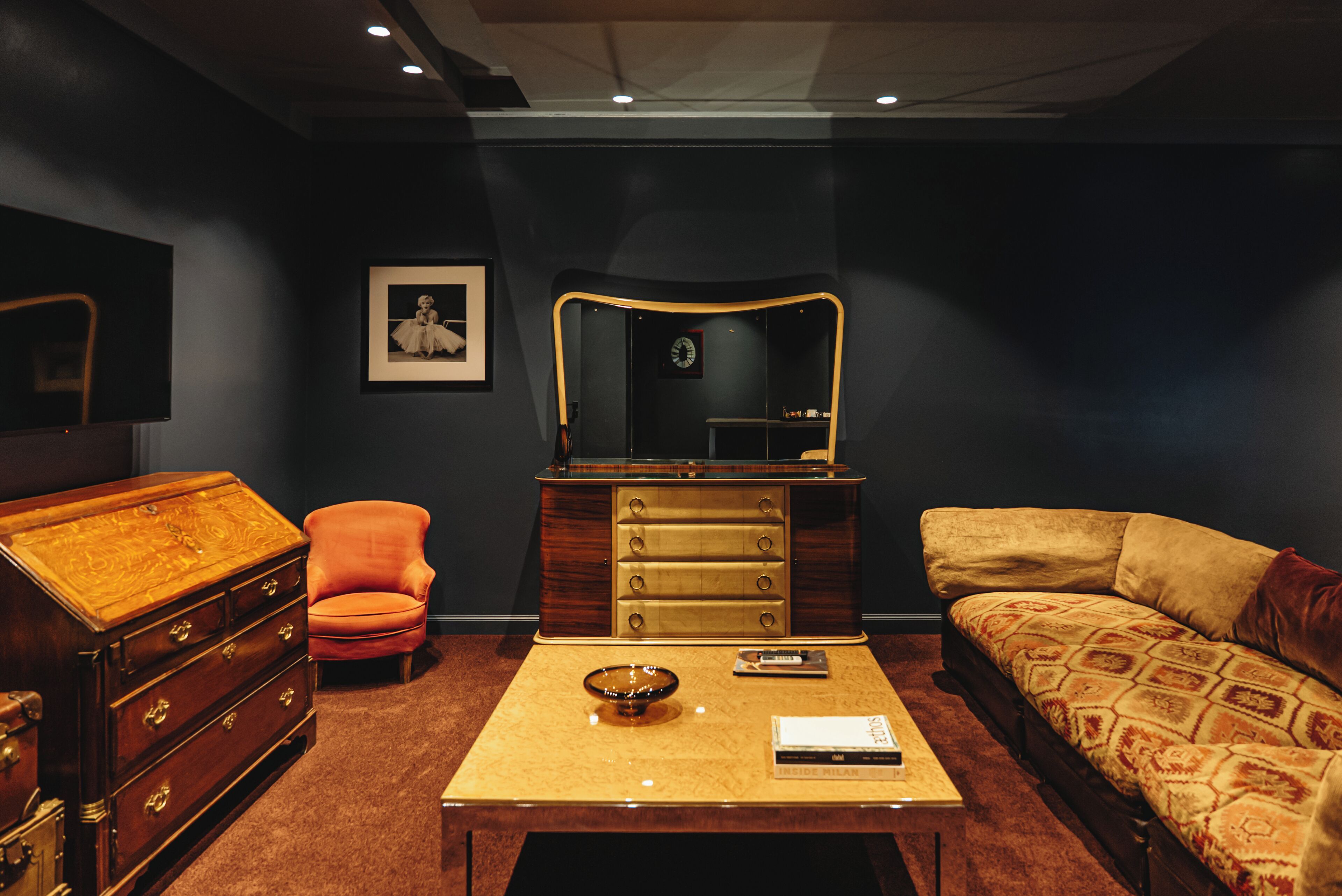 A room with a wooden dresser, a red armchair, a sofa, a coffee table, and a framed picture on the wall.