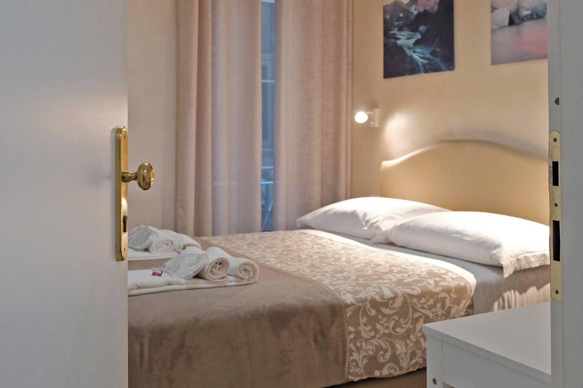 Een slaapkamer met een bed, nachtkastje, hanglamp en een deur met een nummer.