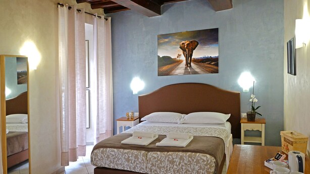 A hotel room with a bed, a painting on the wall, a bedside table with a lamp, and a small potted plant. - Re Monti Guesthouse (Rome)