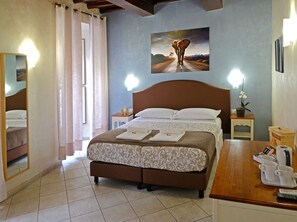 A hotel room with a bed, a painting on the wall, a bedside table with a lamp, and a small potted plant. - Re Monti Guesthouse (Rome)