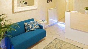 A room with a blue sofa, a small round table, a mirror, a radiator, and a reception desk. - Re Monti Guesthouse (Rome)