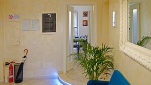 A hotel lobby with a blue sofa, a mirror, a plant, and a fire extinguisher. - Re Monti Guesthouse (Rome)