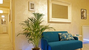 A living room with a teal sofa, a potted plant, and a large mirror on the wall. - Re Monti Guesthouse (Rome)