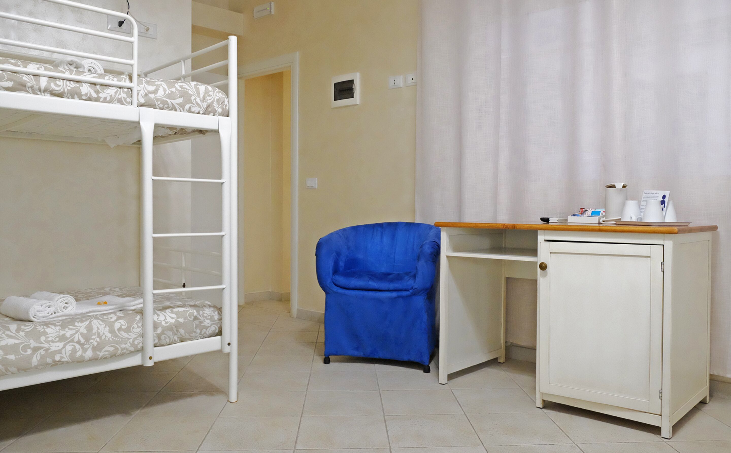 Une chambre avec un lit superposé, un bureau et une chaise, un placard et un rideau.