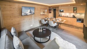 A modern living room with a sofa, a round coffee table, and a dining area with a table set for four. - Good Value Apartments by MX Zermatt (Zermatt)