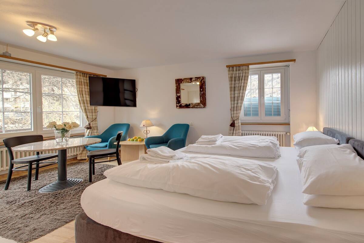 A hotel room with a bed, two chairs, a table, a TV, and a window with curtains.