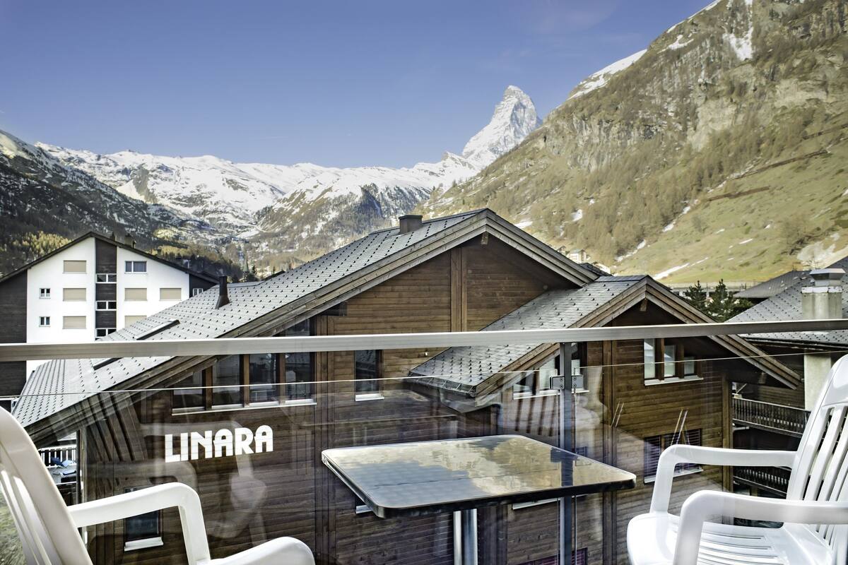 A mountain view with a wooden cabin and a glass table with chairs.