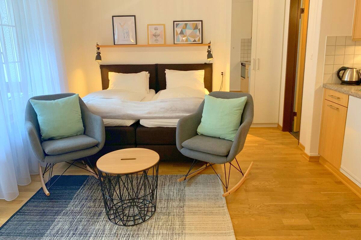 A bedroom with a bed, two armchairs, a small round table, and a headboard with wall art.
