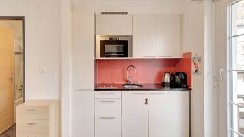A compact kitchen with white cabinets, a stainless steel sink, and a microwave.
