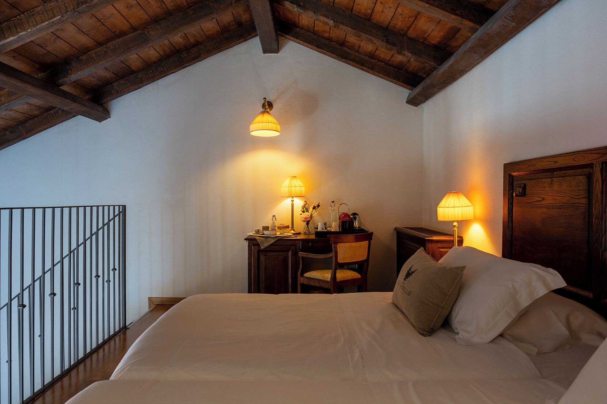 Un dormitorio con una cama, dos mesitas de noche con lámparas, un escritorio con silla y una puerta de madera.