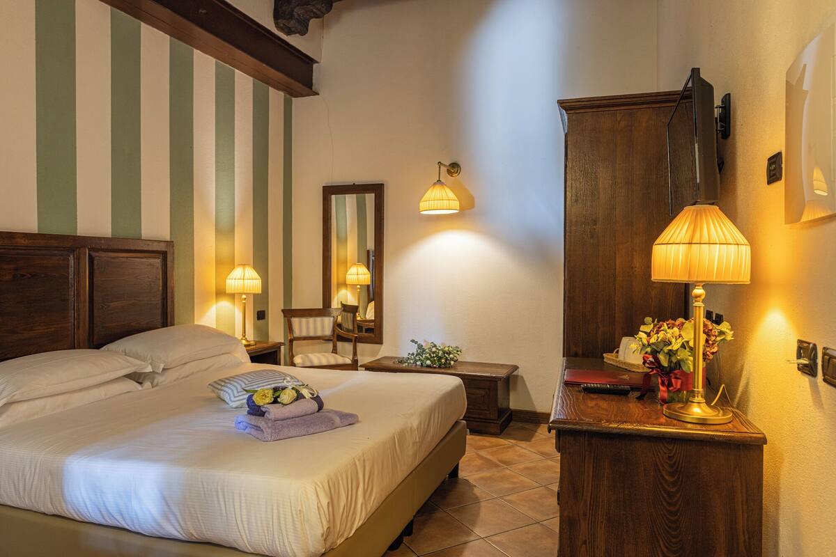 Una habitación de hotel con una cama grande, dos mesitas de noche, un armario de madera y un espejo.
