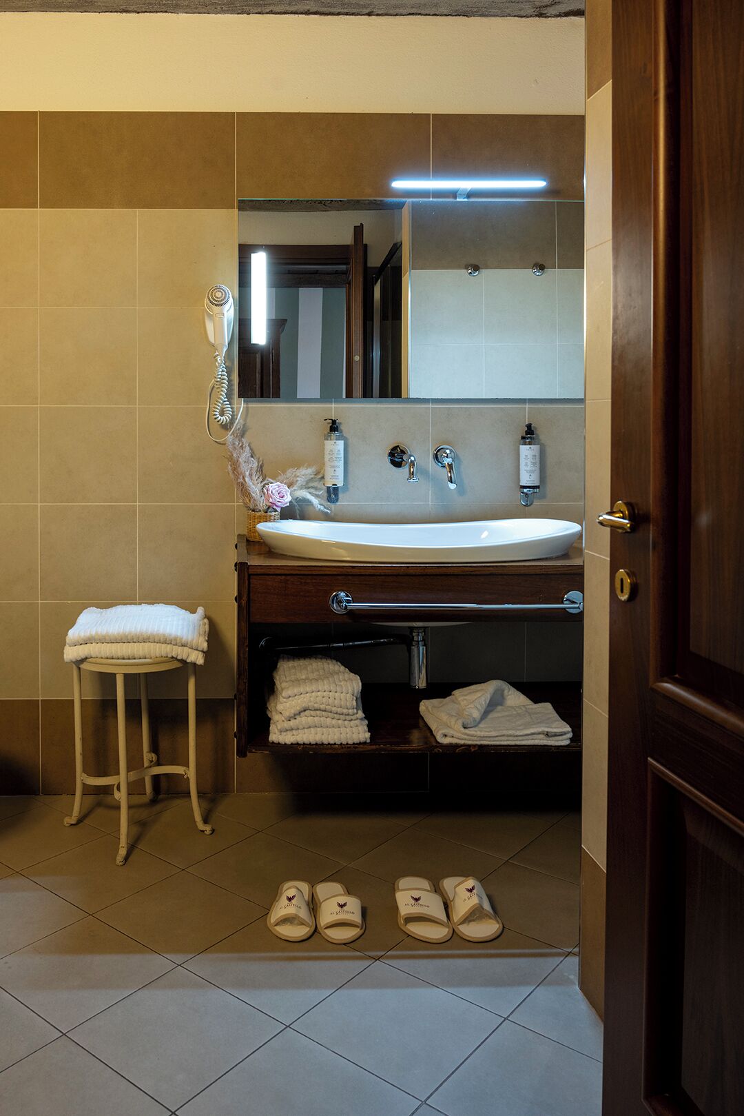A bathroom with a sink, mirror, towel rack, and a pair of slippers on the floor.