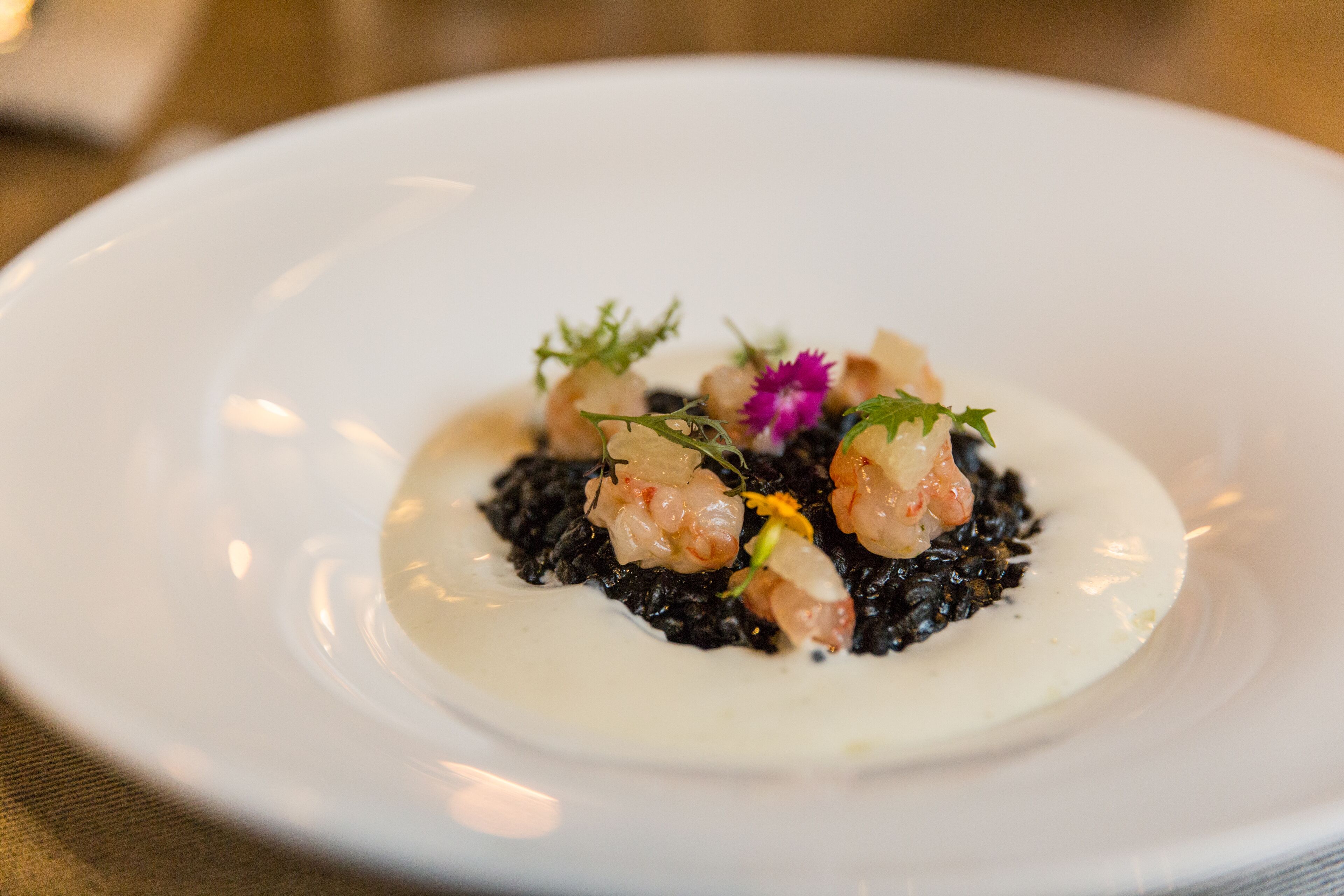A white plate with black risotto, shrimp, and garnishes.