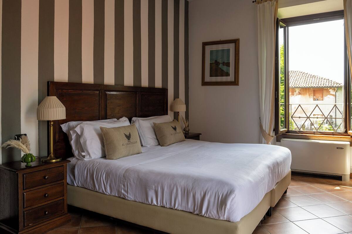 Una cama bien hecha con sábanas blancas, cabecera de madera y dos lámparas de noche.