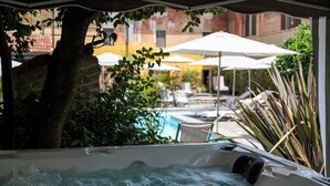 Un jacuzzi con vista a un área de piscina, sombrillas y sillas de descanso.