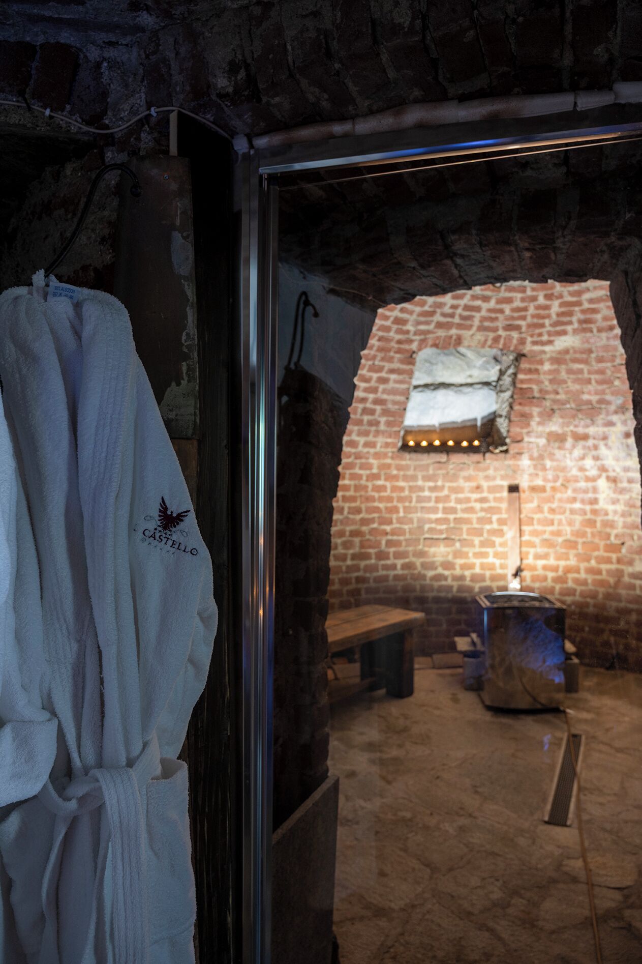 A stone-walled room with a bench, a table, and a towel rack with a robe.