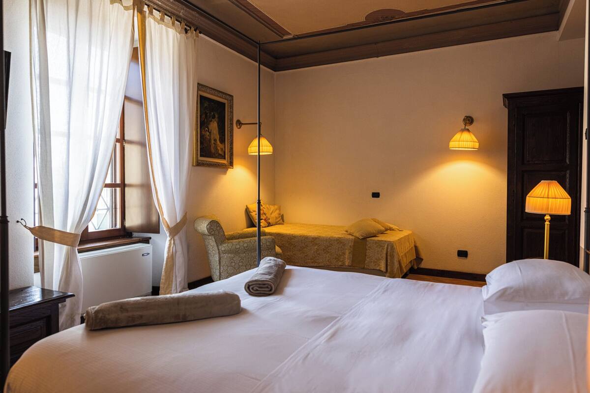 Una habitación de hotel con una cama grande, una silla, una mesita pequeña y dos lámparas fijadas a la pared.