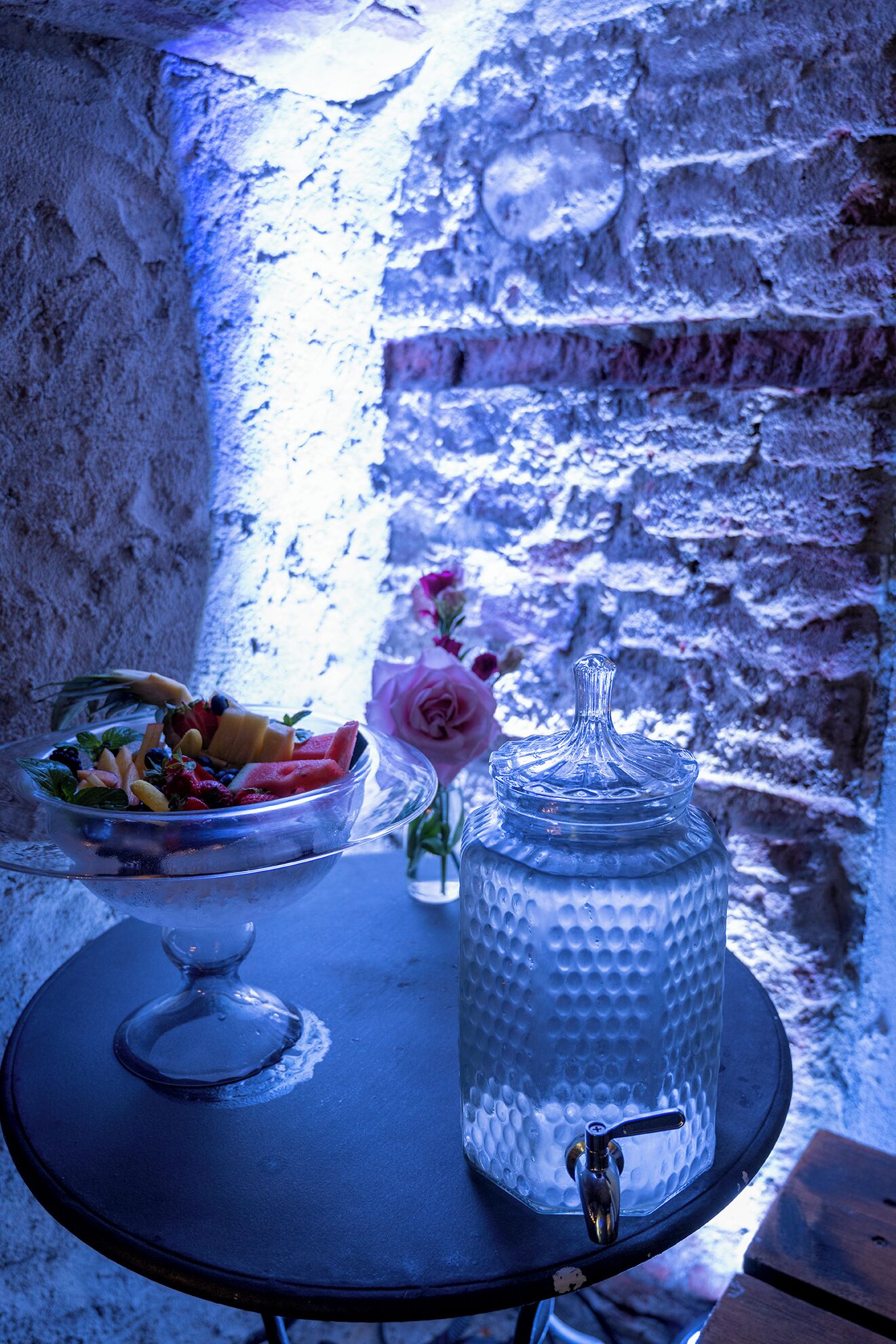 A table with a fruit bowl, a vase with a flower, and a water dispenser.