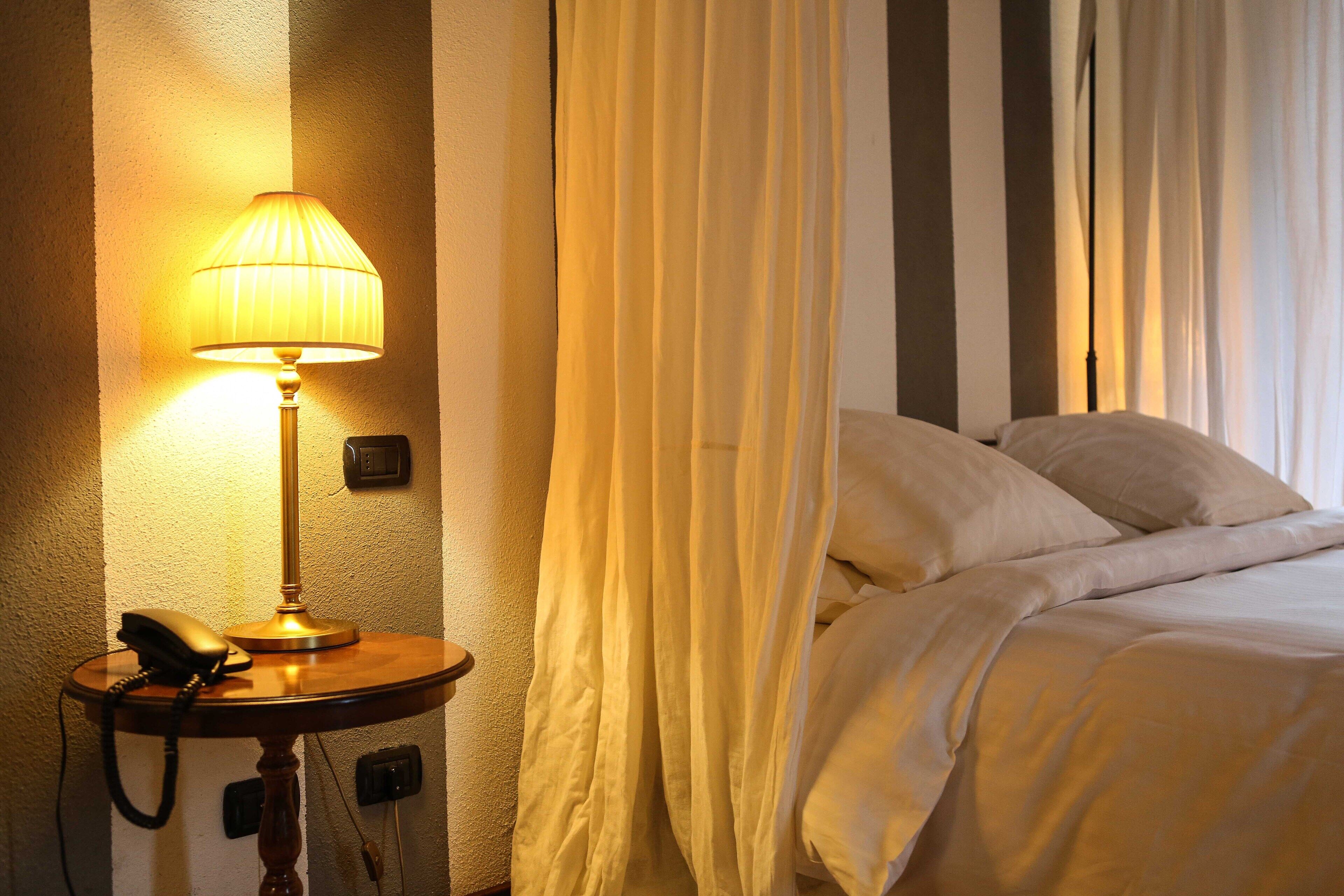 A hotel room with a bed, a bedside lamp, a telephone, and a curtain.