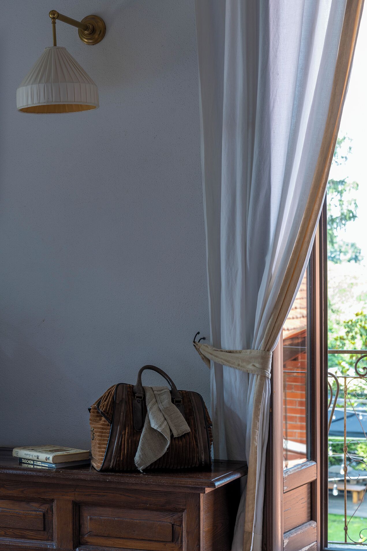 A room with a wooden dresser, a lamp, a handbag, and a window with curtains.
