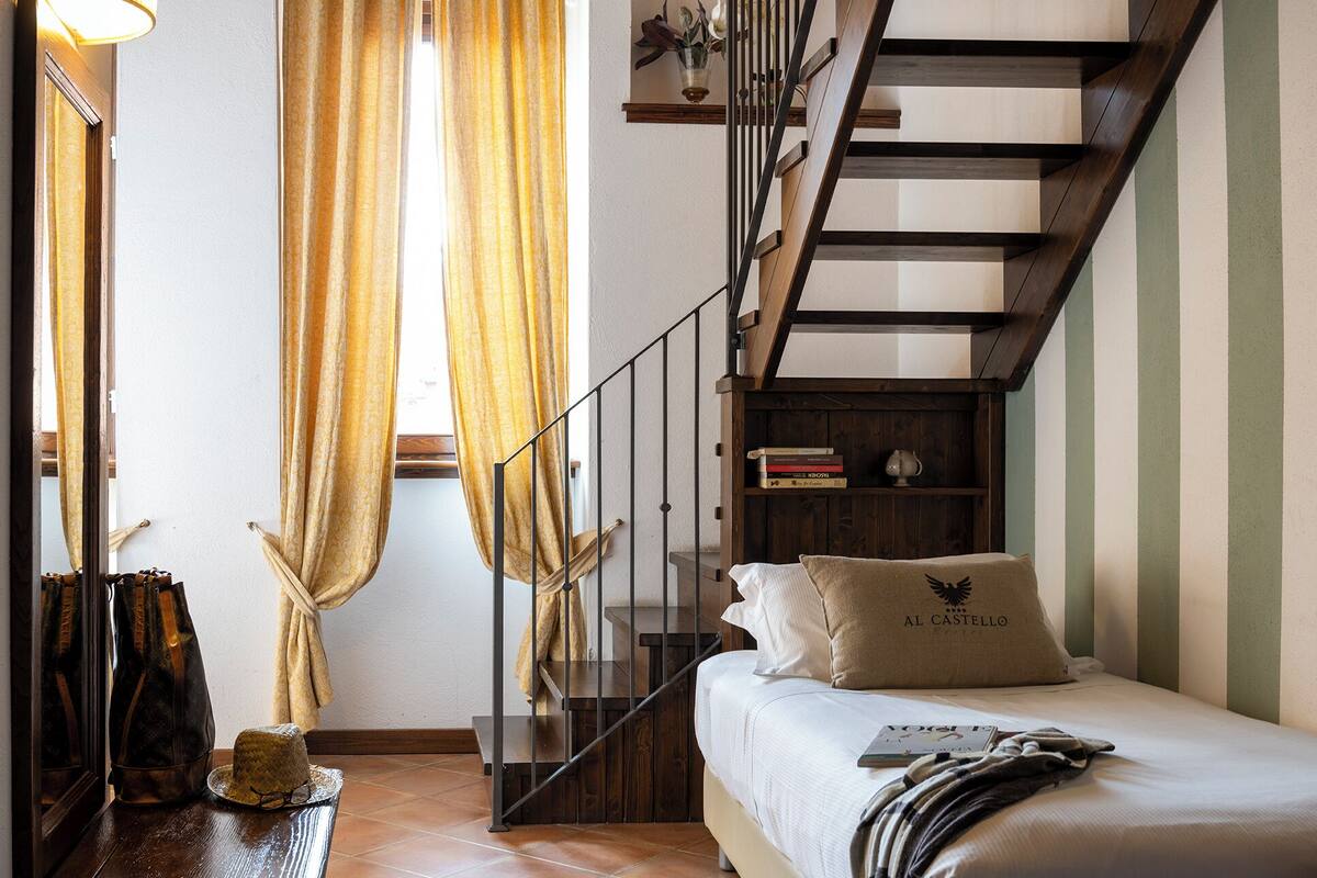Un dormitorio con una cama, una escalera de madera, una estantería y un ventanal con cortinas.