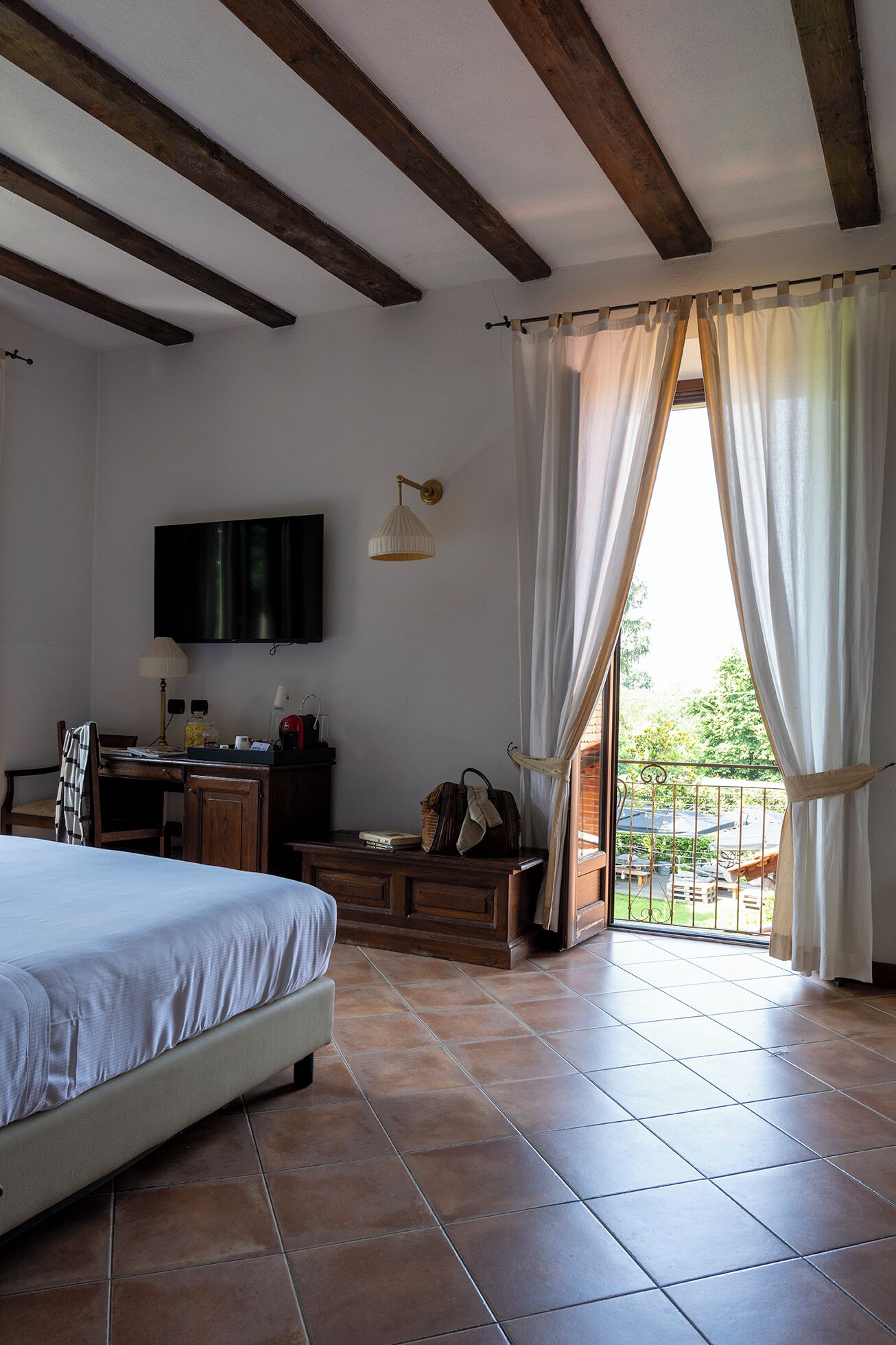 A bedroom with a bed, a desk, a TV, and a balcony with curtains.