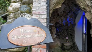 Letrero que dice 'Hammam Emotional Shower', con una rústica pared de piedra y una entrada iluminada en azul.
