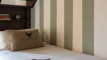 A bedroom with a wooden staircase, a bed with a pillow labeled "AL CASTELLO", and a magazine on the bed.