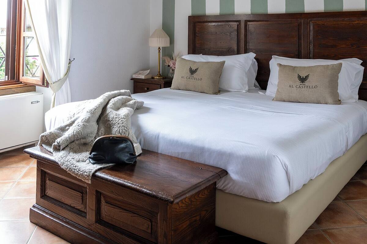 Un dormitorio con una cama grande, una mesita de noche de madera, una lámpara y una ventana con cortinas.