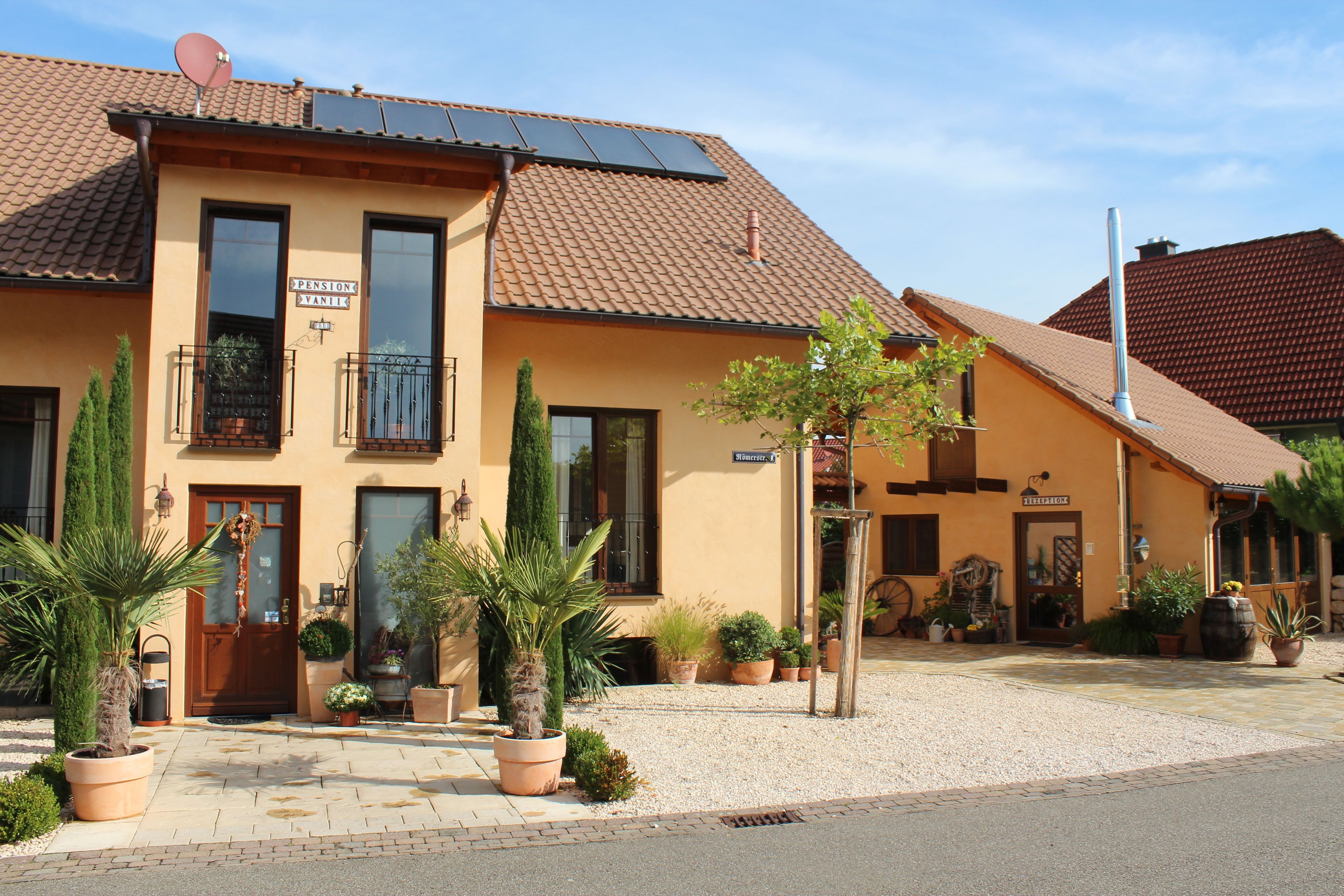 A two-story building with a tiled roof, solar panels, and a sign indicating a pension.