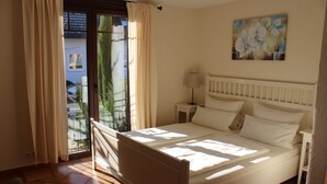 A bedroom with a bed, a nightstand, a lamp, a painting on the wall, and a view through a window with curtains. - Pension Vanii (Rust)