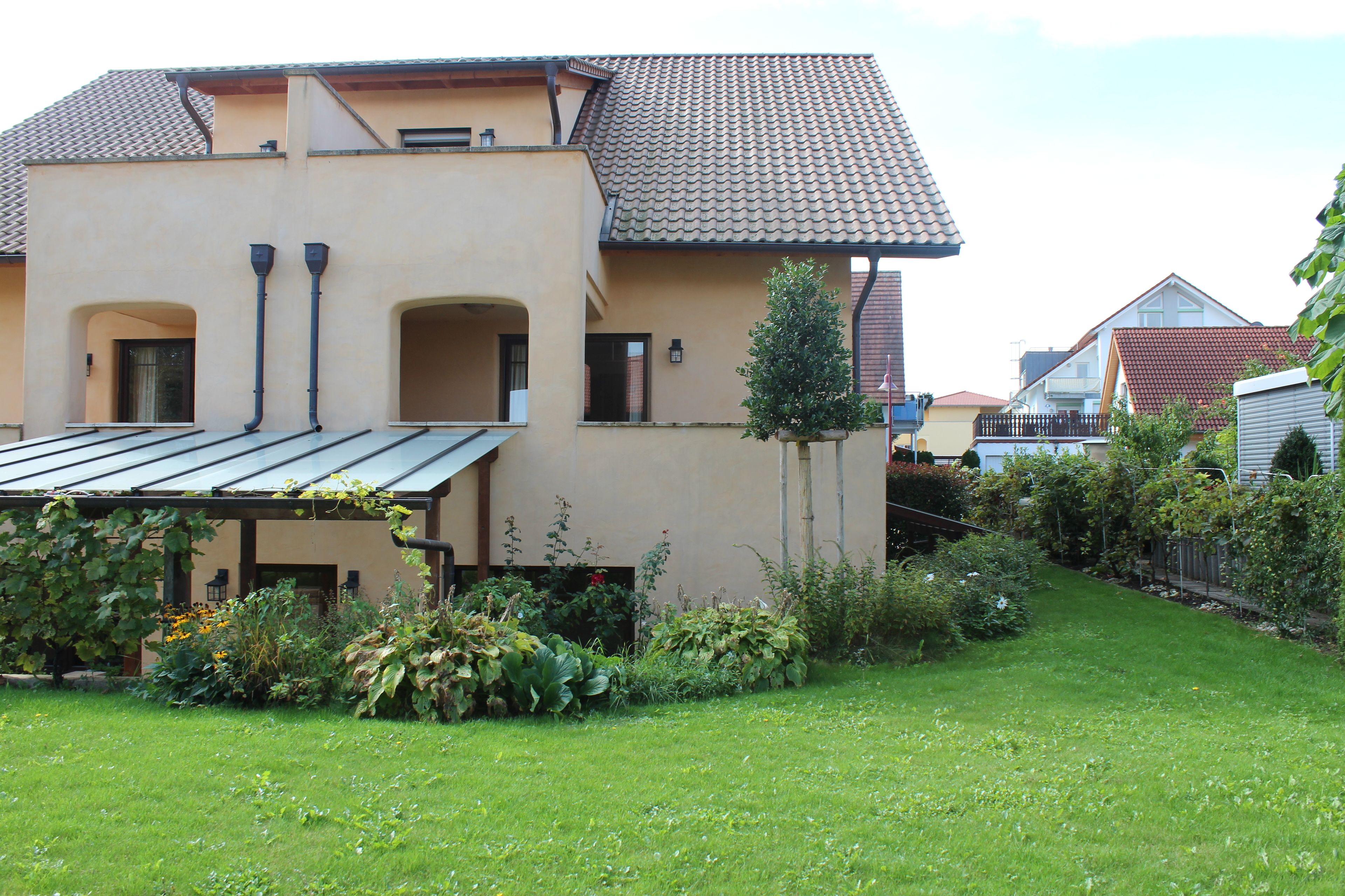 A two-story house with a tiled roof, a covered patio, and a well-maintained garden.