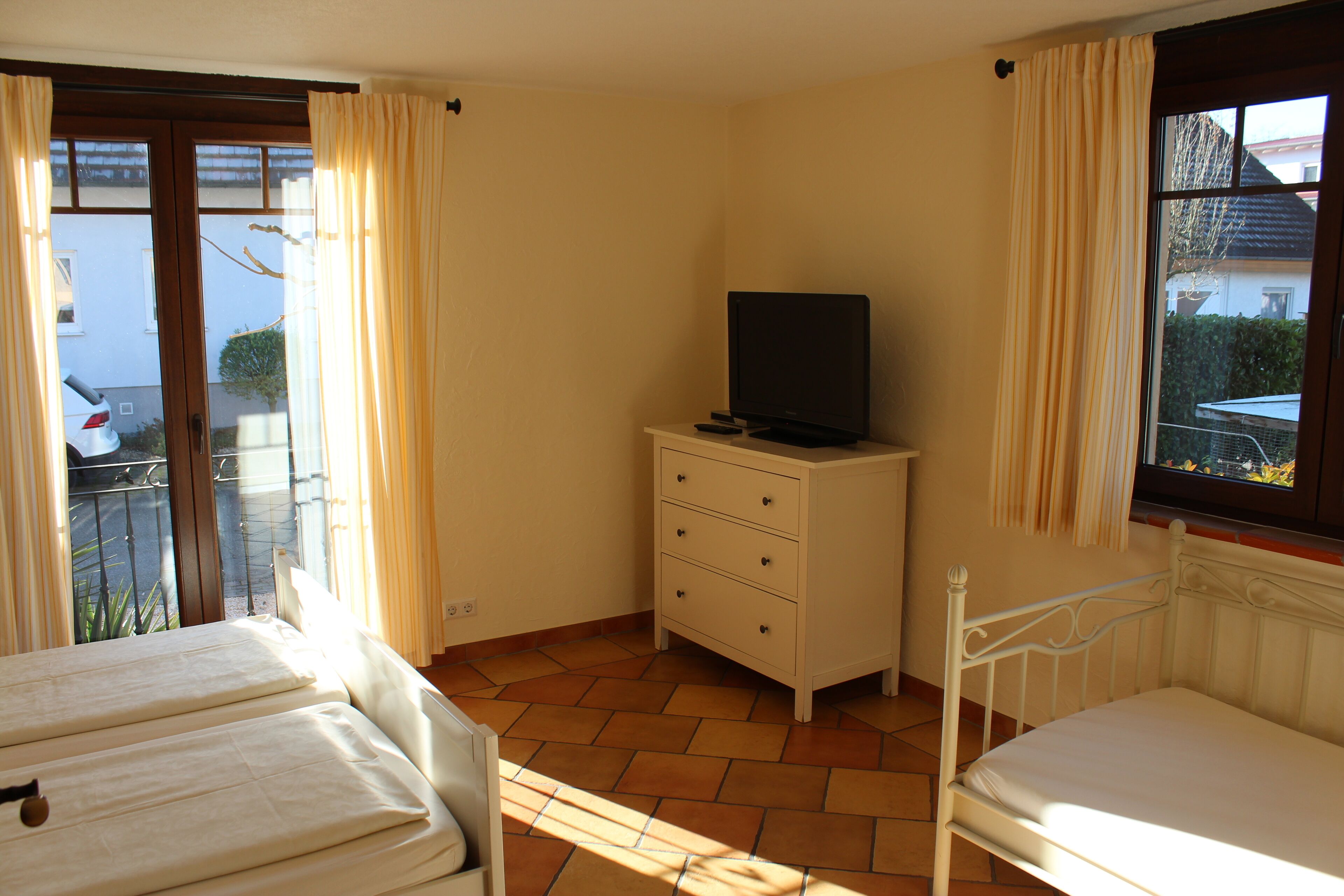 A bedroom with two beds, a dresser, a television, and a window with curtains.